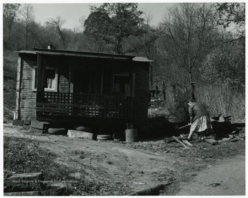 A woman chopping wood outside of her home.