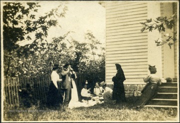 A group of unidentified  men and women gathered for dinner on the ground outside a church.  One woman seems to be dressed in mourning attire. From the Ellison-Dunlap families collection, Monroe County.