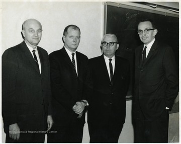 A portrait of Ernest Nesius standing with three other men in a classroom.