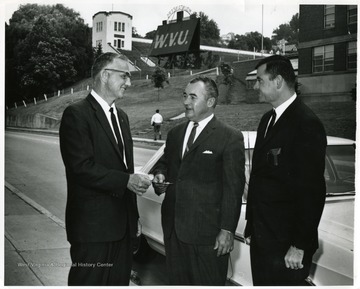 Pete Yost (left), Dean of Physical Education, standing with two other men outside Old Mountaineer Field.