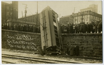 A street car fell down on railroads track, onlookers gather around.