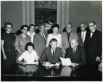 A group photograph inside E. Moore Hall including J.O. Knapp (third from right, back row), Charles Bissett (seated, center) and Mrs. H.D. McGinnis (second from left, standing).