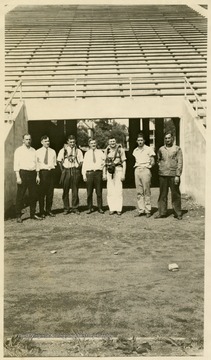 A portrait of seven men, two in safety gear, standing in a stadium, likely old Mountaineer Field.