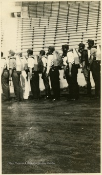 A group of men wearing safety gear lined up inside of a stadium, likely Mountaineer Field.