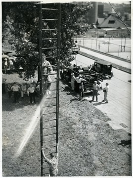 A man on a ladder during safety training.  WVU Tennis courts on Beechurst Avenue visible. 