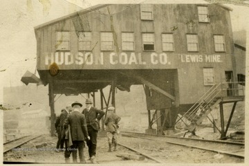 A photograph of a group of men standing on the railroad tracks under a Hudson Coal Company building at the Lewis Mine.