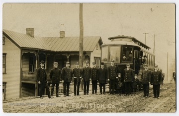 Workers of Grafton Traction company with a car in the background and passengers.