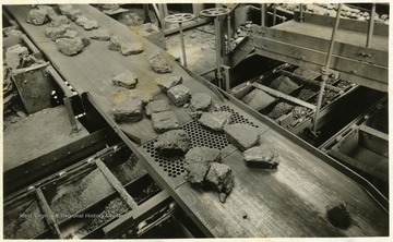 A photograph of coal moving along a conveyor belt and over a grate. 'Island Creek Coal Sales Co., Cincinnati, Ohio; The following cars of Pocahontas coal were shipped today for account of; P.C. Pocahontas Coal'