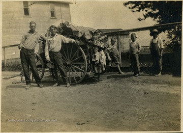 Unidentified men and children pose with a carriage full of lumbers and others.