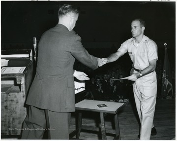 A photograph of a military man with the last name Hickman on stage receiving what appears to be an award of some sort.
