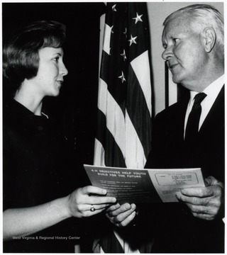 A photograph of the Honorable Harley Staggers (right) presenting a booklet to Martha Poland.