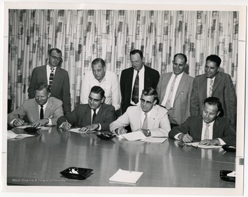 "Merger Agreement Signed- Culminating months of negotiations between W. Va State Federation of Labor (A.F.L) and the W. Va State Industrial Union Council (C.I.O), representatives of both groups formally sign an agreement on September 24, 1957 which paved the way for the merger convention on November 22, 1957. Shown (seated, left to right) are Benjamin W. Skeen, S.F.L secretary-treasurer; E. A. Carter, S.F.L president; Oscar L. Davis, I.U.C president and Miles C. Stanley, I.U.C secretary treasurer;(standing, left to right) Rene V. Zabeau and James Q. Papas, S.F.L vice-presidents; Rezin Hudkins, John Lambert and Charles Hess, I.U.C vice-presidents."