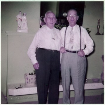 A photograph of two unidentified men standing in front of a mantle.