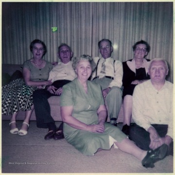 A photograph of an unidentified group of men and women seated in a living room.
