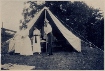 A photograph of a man and three women gathered around a camp site.