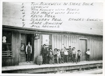 Left to right:  1) Tom Blackwell in the Store Door, 2) Unknown, 3) Tom Kenney with Beard, 4) Bob Haley with Boots, 5) Kelso Dell, 6) Scrubby Dell, 7) Babe Johnson, 8) Bill Nichols, Others Unknown.