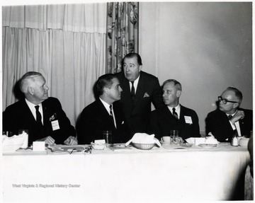 A photograph of Senator Jennings Randolph (standing) behind Harley Staggers (left), Sargent Shriver (second from left), Paul Miller (second from right) and Don Bond (right). 
