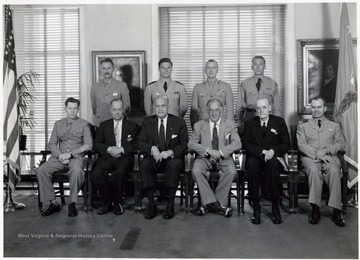 'Sitting, Left to Right: Lt. Colonel A. W. Tyson, USA, Dr. Philip E. Adams, Honorable Louis Johnson, Honorable Stephen Marly, William F. Gibbs, Commander John P. Floyd, USNR; Standing, Left to Right: Lt. Colonel H. L. Conner, USA, Lieutenant (jg) Theodore Hartley, USN, Lt. Colonel Roy L. Kline, USMC, Major Paul Kendall, USAF.'