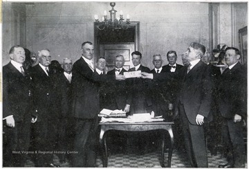 'W. S. Johnson, treasurer of West Virginia, presenting to Judge Rhea, attorney general of Virginia. West Virginia's check for $1,078,000, on account of the Virginia debt, in room 534, Willard hotel, Washington, D.C., Friday, April 18. Immediately behind Mr. Johnson stands E. T. England, attorney general of West Virginia. The others of the party are members of the Virginia dept commission and lawyers employed by that commission.'