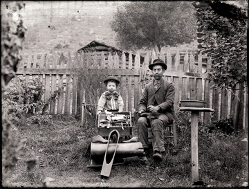 A portrait of man and boy with shoe making supplies and tools; the photo taken in the back yard, Helvetia, W. Va.