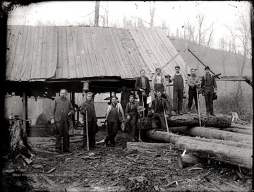 A portrait of loggers with tools in front of lumber mill in Helvetia, W. Va.