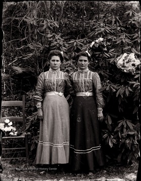 A portrait of two women in the garden near a rhododendron tree.