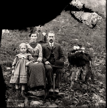 A man, woman, and two children pose by a tree stump with hats and garments on it.