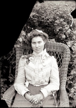 A portrait of woman in wicker chair taken outdoors.