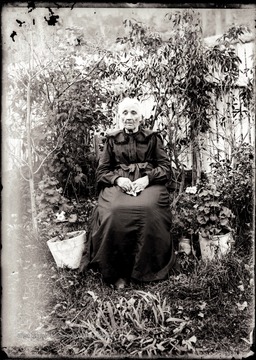 A portrait of an elderly woman sitting against a fence.