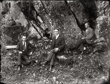 A portrait of three men sitting in front of rock ledge.