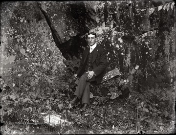 A portrait of man sitting at the rock ledge.