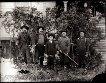 Four men and a boy holding guns taken outside of a house.