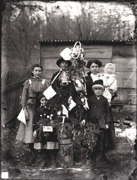 On the left of the tree is Bess Shock and Cinderilla Shock standing in front of her.  Behind the tree is Dan Halderman, a neighbor of the Shock family.  On the right side of the tree is Alma Shock holding baby, Charles R. Shock.  Standing in front of Alma and Charles is brother, Herbert Shock.