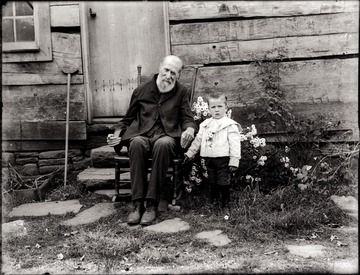 A portrait of seated old man and boy taken just outside of the house in Pickens, W. Va.