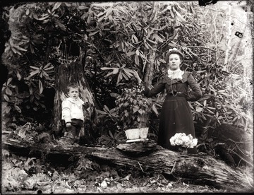 A portrait of woman and boy standing under rhododendron trees.