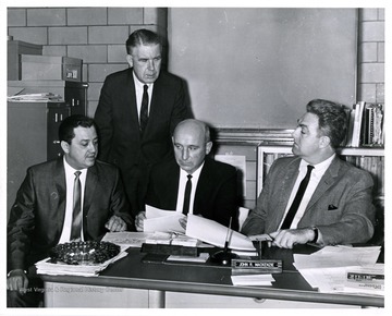 Four men in a room; the center man is identified as John R. McKenzie.