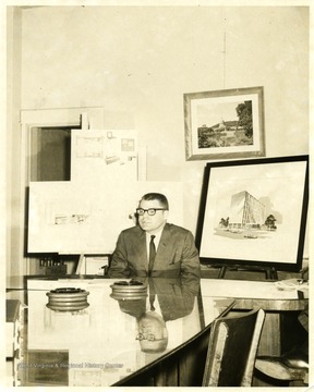 An unidentified male sits in front of architectural drawings. 