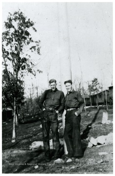 Two males stand in front of an erect pole.