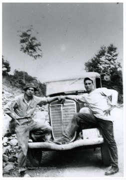 Two males pose with their foot up on the bumper.
