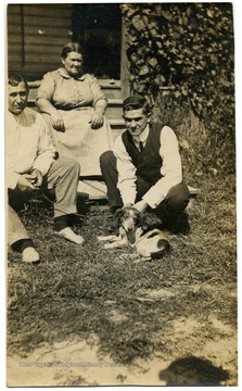Two unidentified men and a woman sitting outside with a dog.