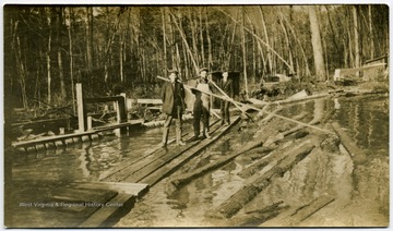 Two men with the long pikes are "poling" logs in the log pond toward the jack ladder which takes the logs into the sawmill.