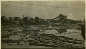 Postcard photograph of a log pond with the lumber mill in the background.