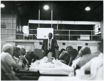 African American man singing at the head of the table.