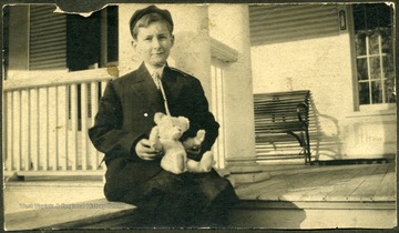 Portrait of a young J. Hammond Siler, Jr. sitting on a front porch with a teddy bear in his lap. 