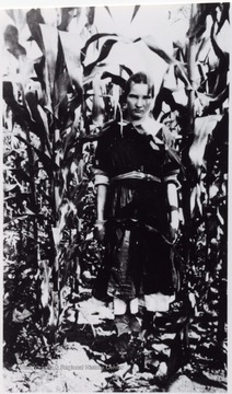 Girl standing in between tall corn stalks.