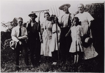 Family posed with pitchforks. Man and woman at each end are holding hats.