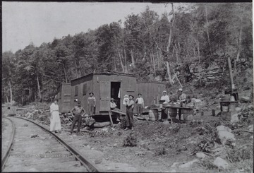 Group posed by railroad tracks. The shanty cars in the background were used by the workers. 