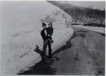 Father and son standing next to a large snow bank.