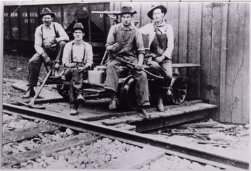 Men seated next to railroad tracks with tools.