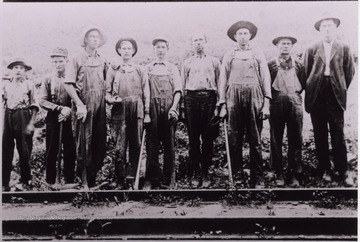 A group of workers posed on the side of train tracks with tools.